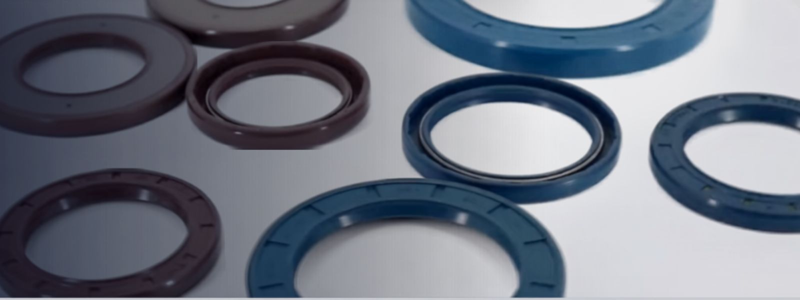 Diversos retentores industriais de vedação em tons de azul, cinza e marrom, organizados sobre superfície metálica reflexiva, close-up macro, iluminação suave e técnica, fotografia realista de produto industrial